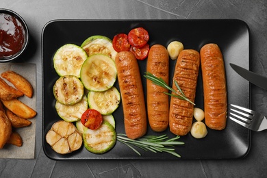 Delicious grilled sausages and vegetables on grey table, flat lay