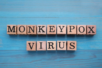 Photo of Words Monkeypox Virus made of cubes with letters on light blue wooden table, top view