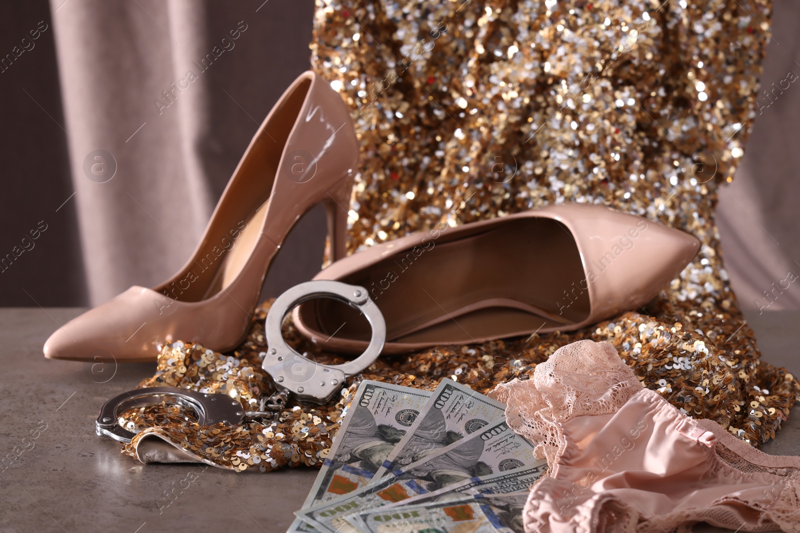 Photo of Prostitution concept. Women's panties, dollar banknotes, handcuffs and high heeled shoes on grey textured table