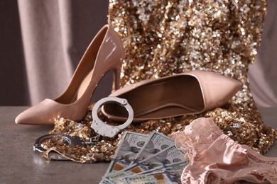 Photo of Prostitution concept. Women's panties, dollar banknotes, handcuffs and high heeled shoes on grey textured table