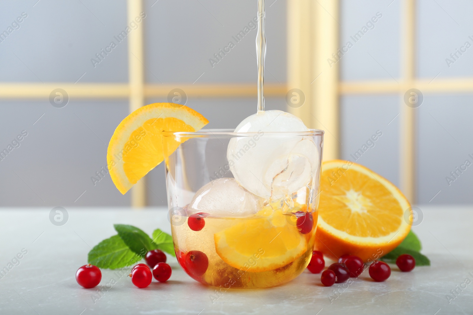 Photo of Pouring tasty cocktail into glass with ice balls at light grey marble table