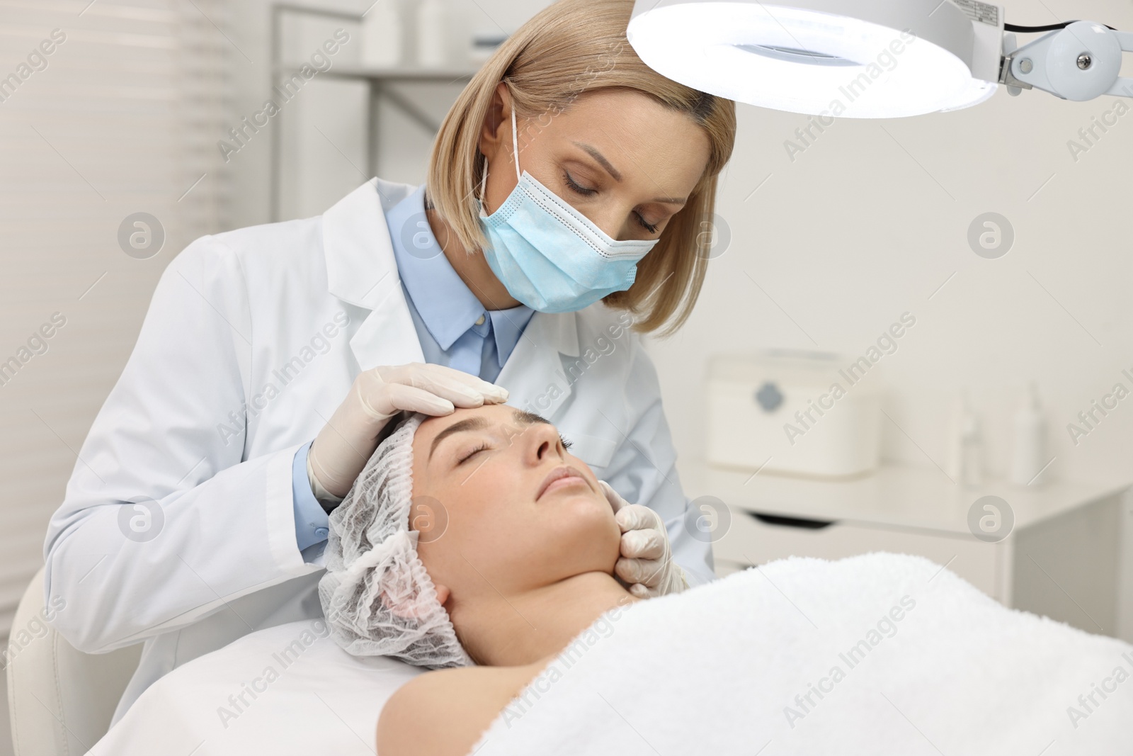 Photo of Dermatologist examining patient`s face under lamp in clinic