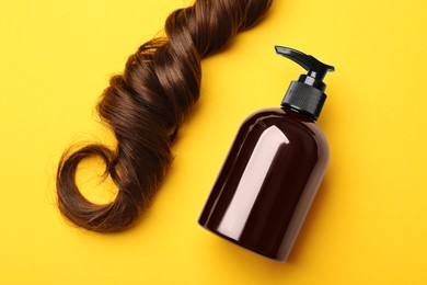 Photo of Lock of hair and shampoo bottle on yellow background, flat lay