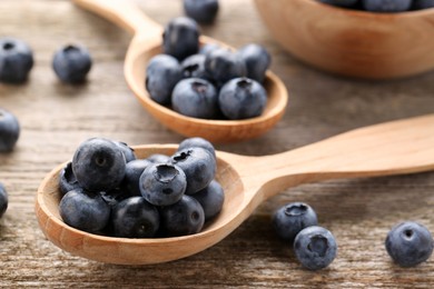 Photo of Spoons with tasty fresh blueberries on wooden table, closeup
