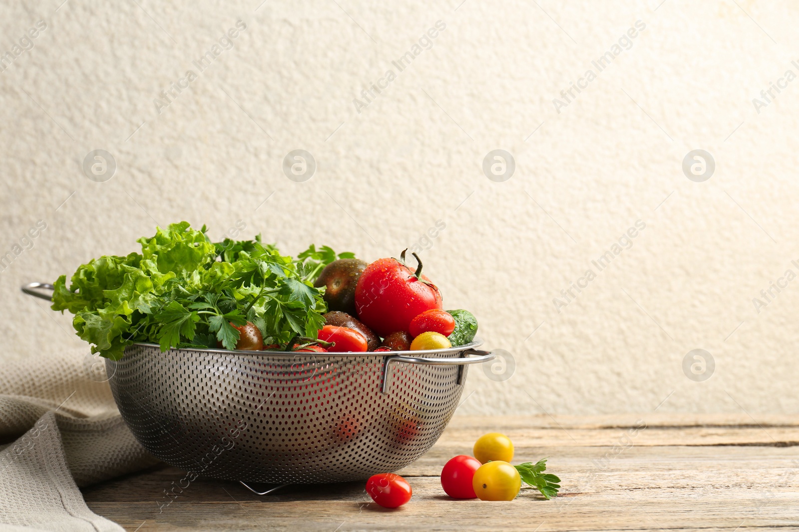 Photo of Wet vegetables in colander on wooden table, closeup. Space for text