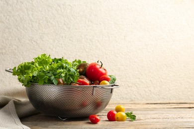 Wet vegetables in colander on wooden table, closeup. Space for text