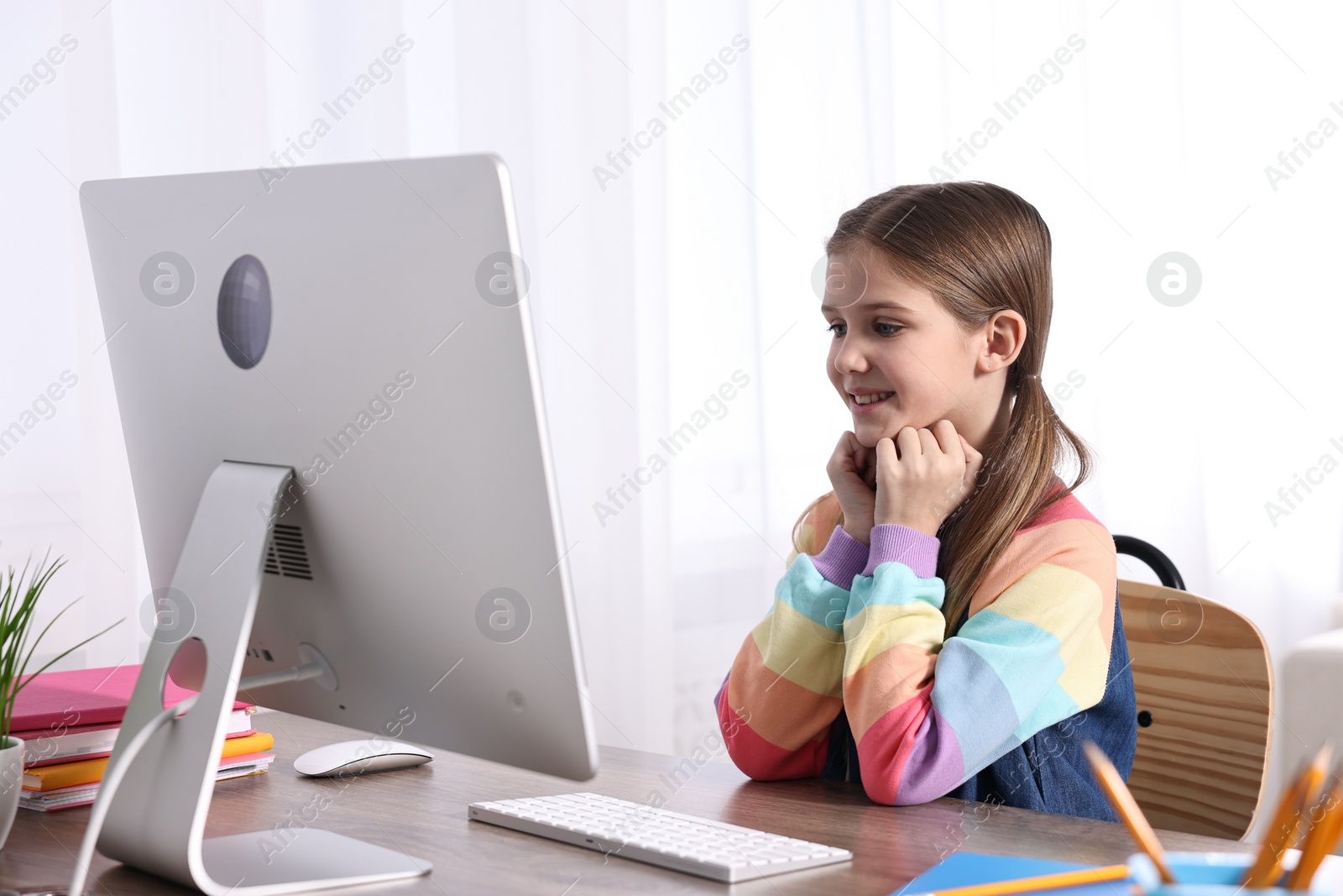 Photo of E-learning. Cute girl using computer during online lesson at table indoors