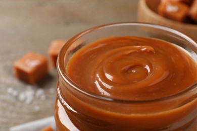 Photo of Yummy salted caramel in glass jar on table, closeup