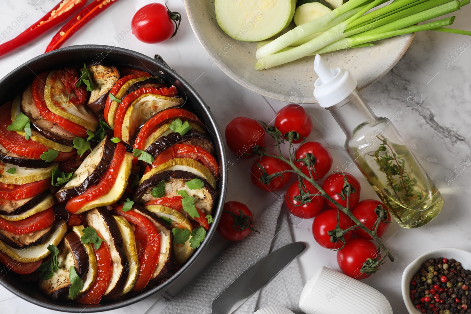 Photo of Delicious ratatouille, ingredients and knife on white table, flat lay