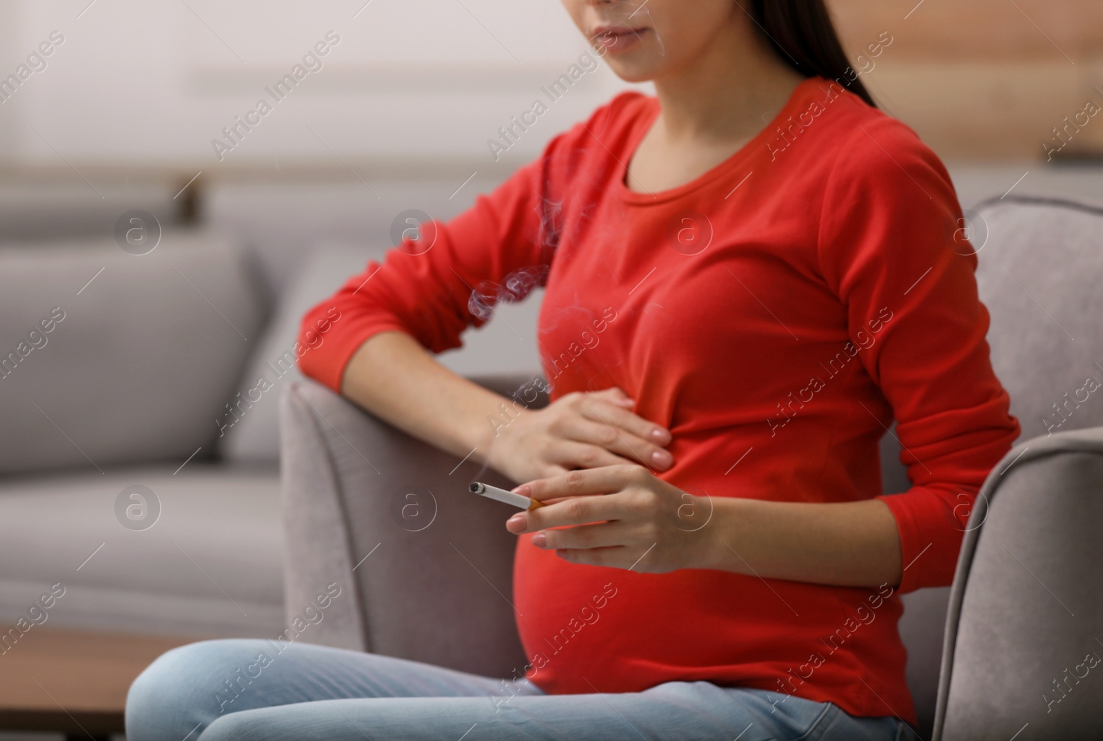 Photo of Young pregnant woman smoking cigarette at home, closeup