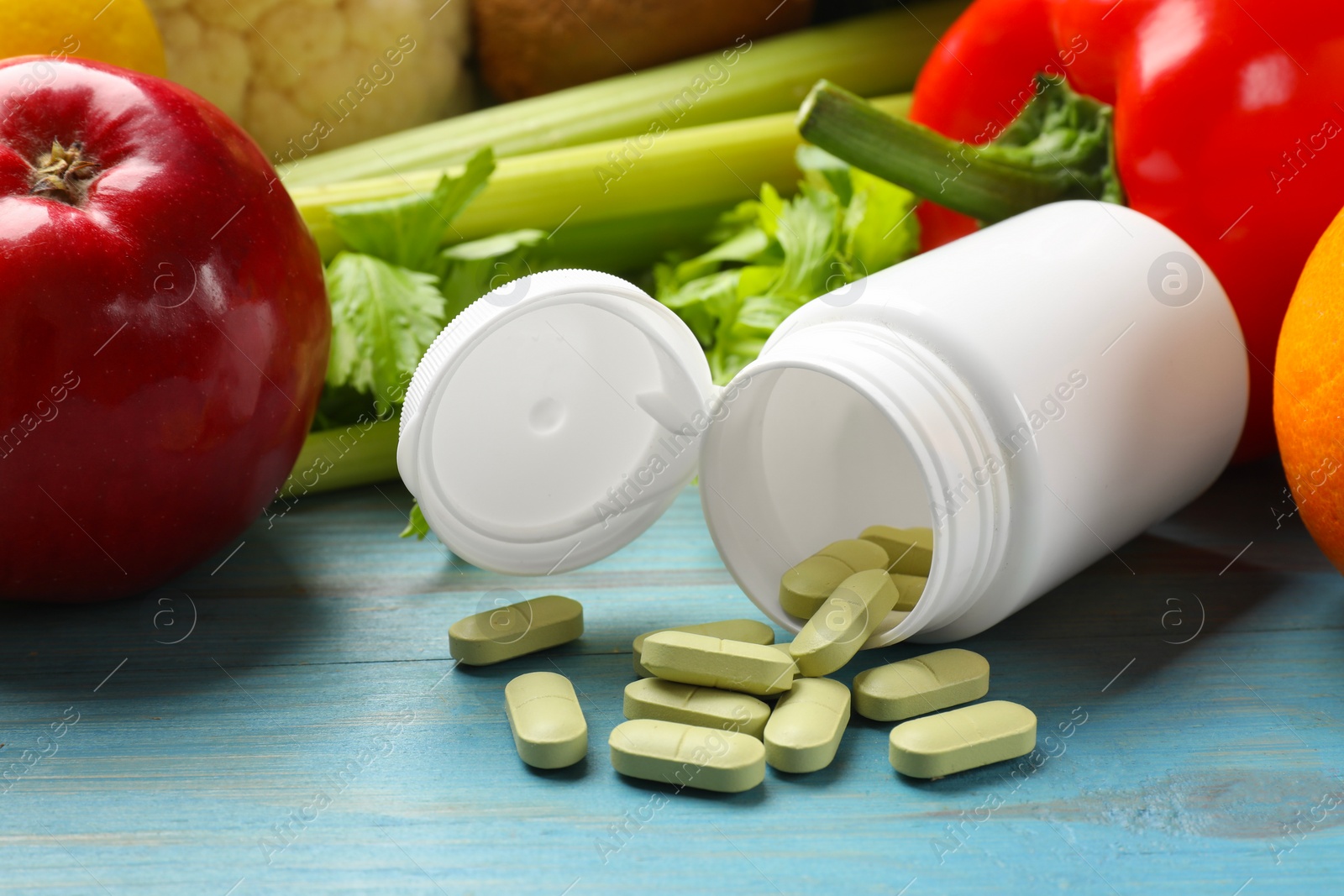 Photo of Dietary supplements. Overturned bottle with pills near food products on light blue wooden table