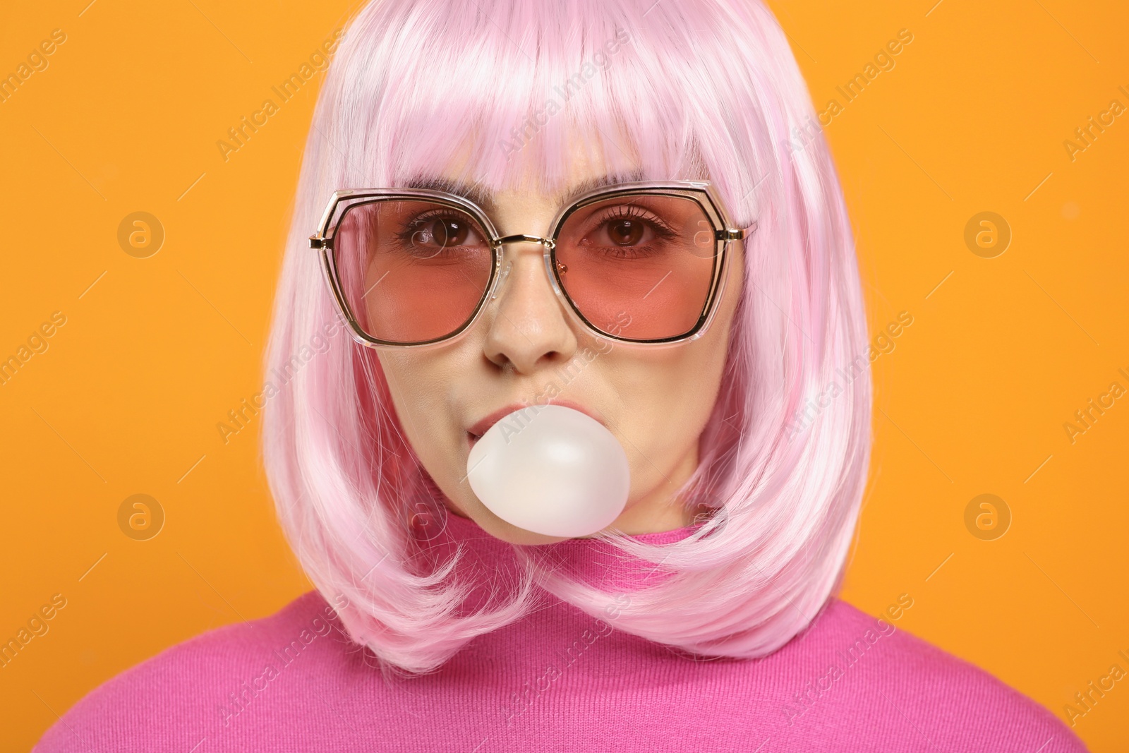 Photo of Beautiful woman in sunglasses blowing bubble gum on orange background