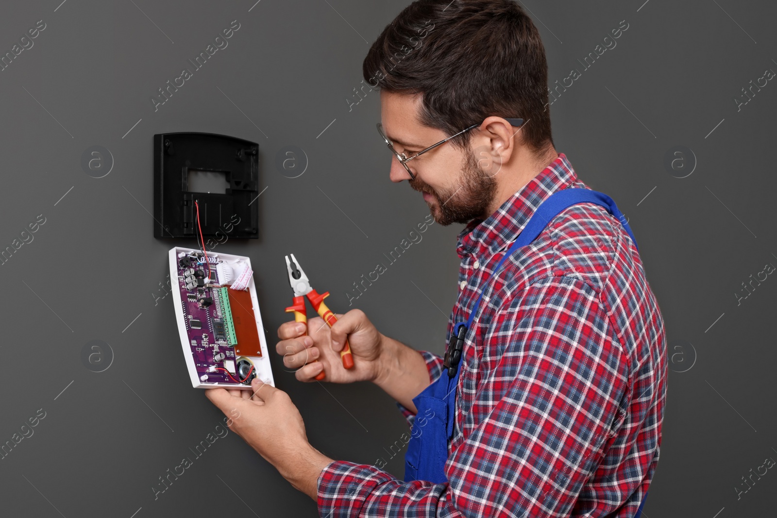 Photo of Technician installing home security alarm system on gray wall indoors