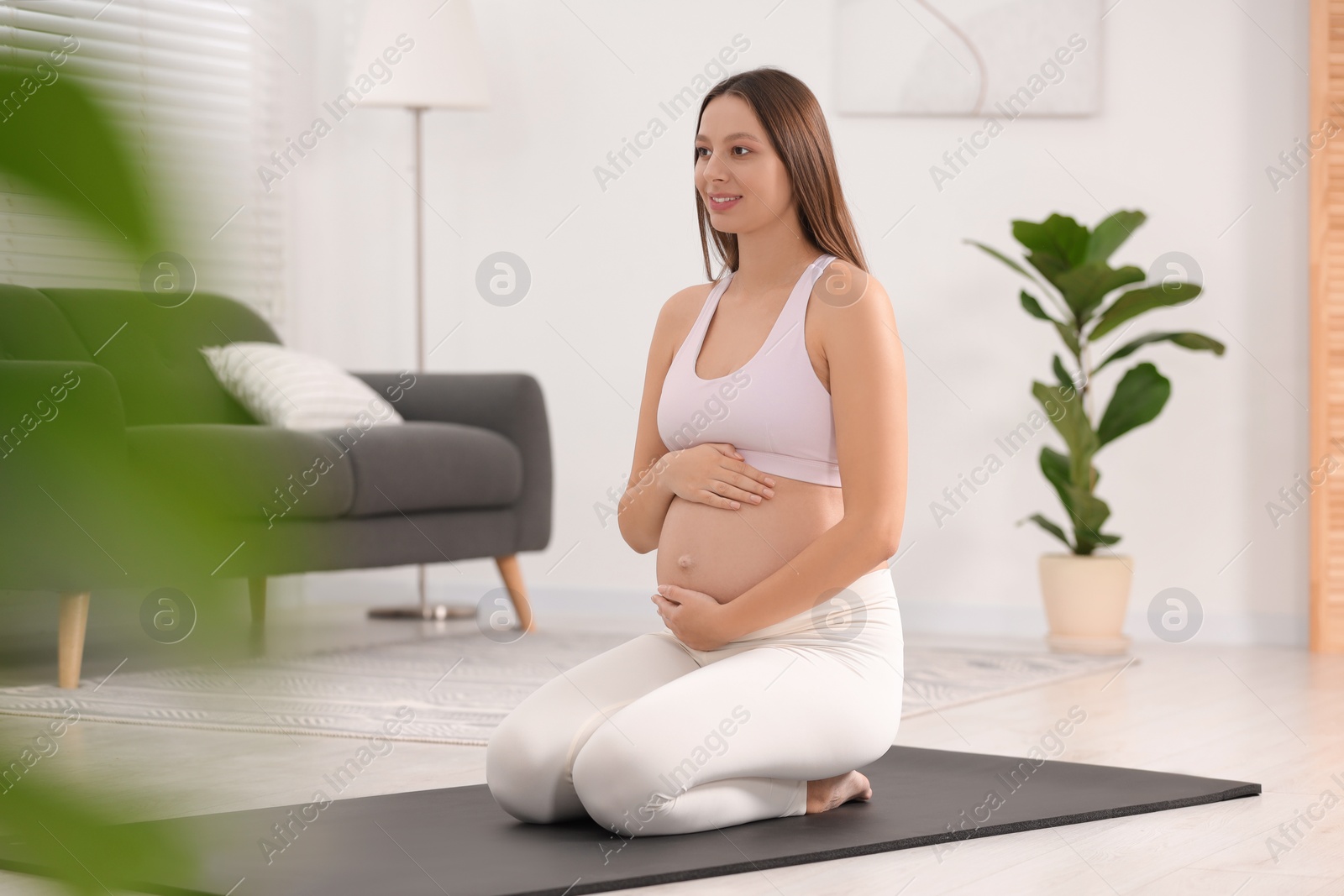 Photo of Pregnant woman sitting on yoga mat at home, space for text