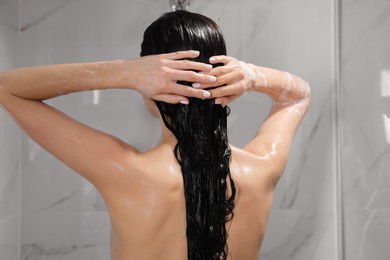 Young woman washing hair while taking shower at home, back view