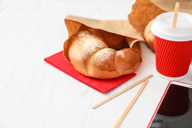 Photo of Cup of coffee, bun in paper bag and smartphone on wooden table