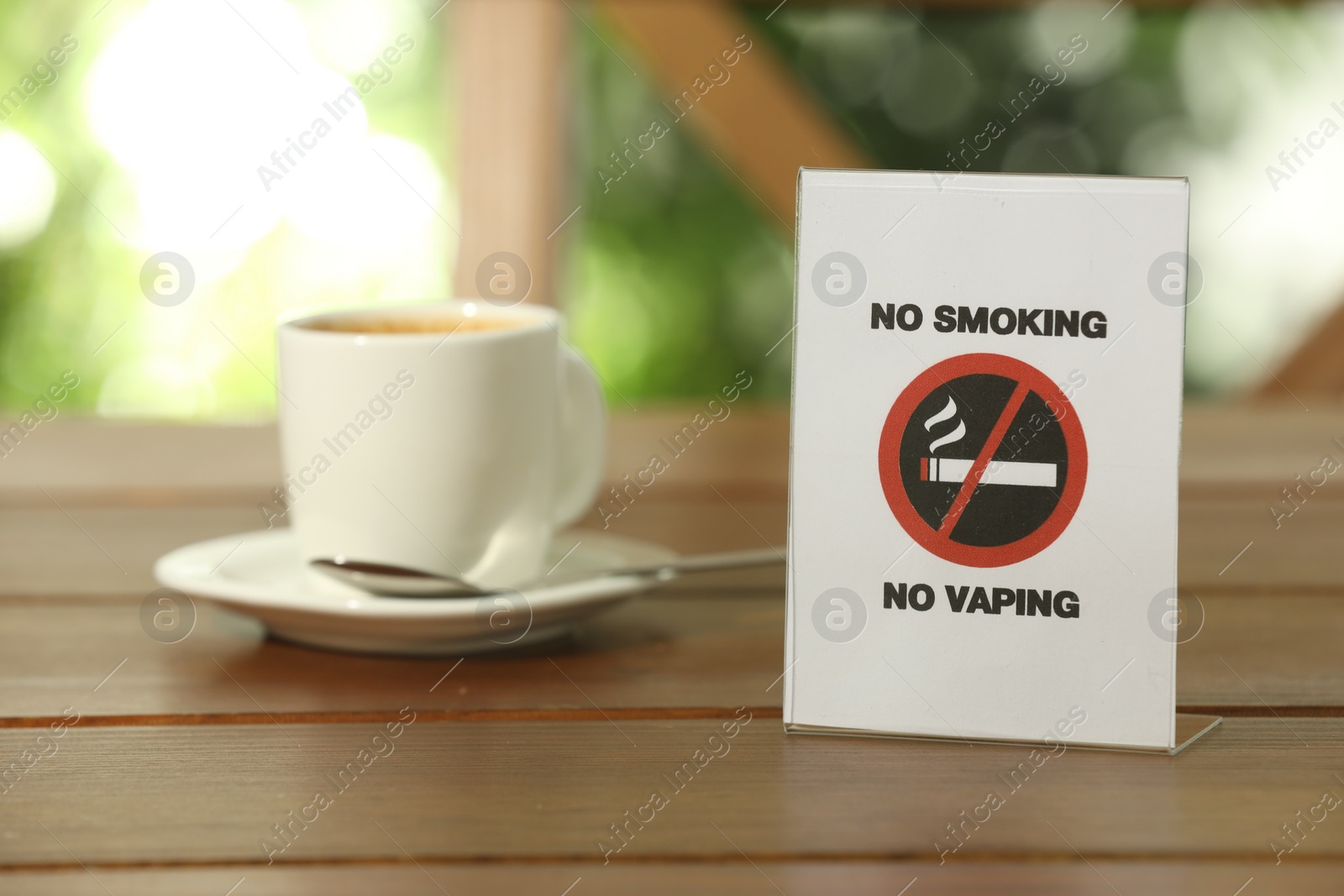 Photo of No Smoking No Vaping sign and cup of drink on wooden table outdoors. Space for text