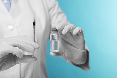 Doctor holding syringe and glass vial on light blue background, closeup. Space for text