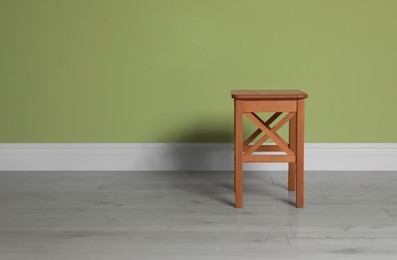 Photo of Stylish wooden stool near light green wall indoors. Space for text