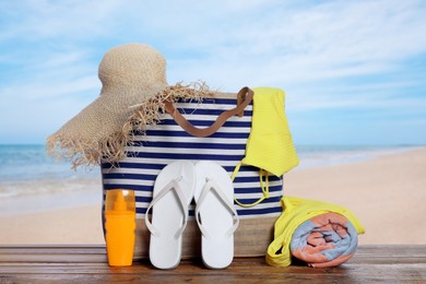 Image of Stylish striped bag and other beach accessories on wooden table near sea