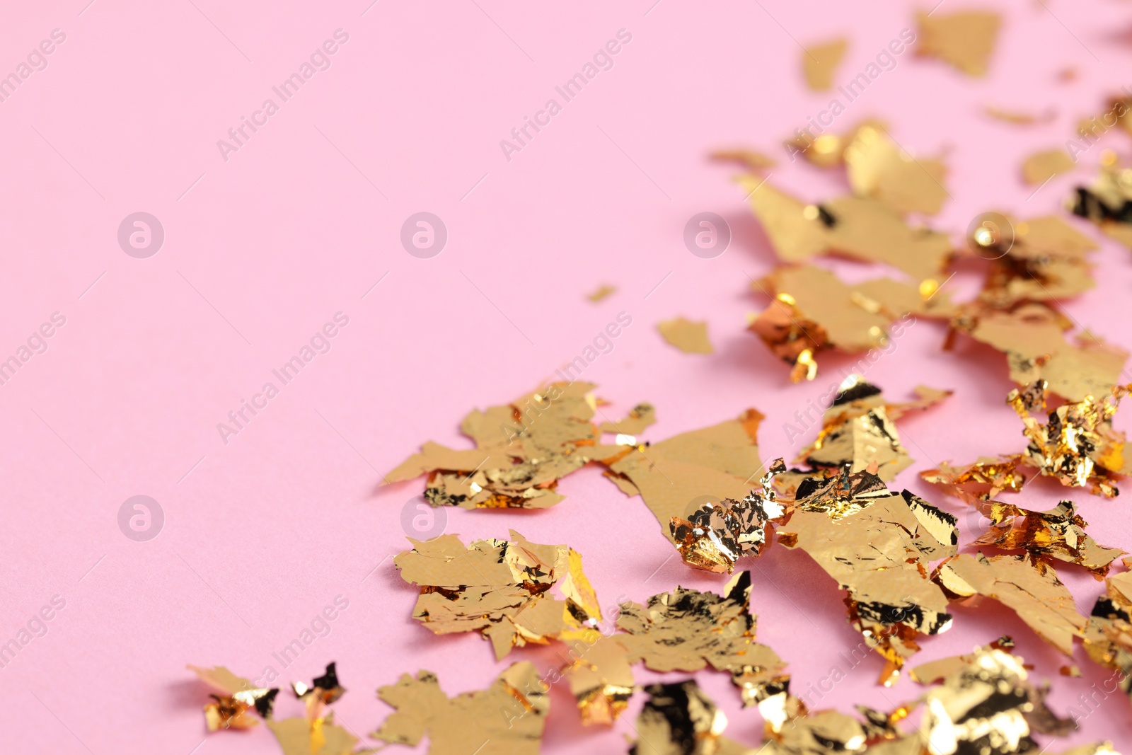 Photo of Many pieces of edible gold leaf on pink background, closeup. Space for text