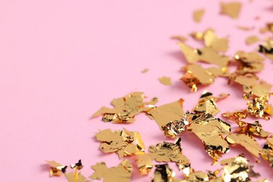 Photo of Many pieces of edible gold leaf on pink background, closeup. Space for text