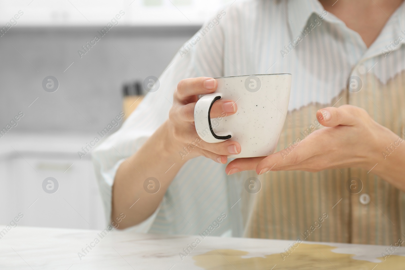 Photo of Woman with spilled coffee over her shirt at marble table in kitchen, closeup. Space for text