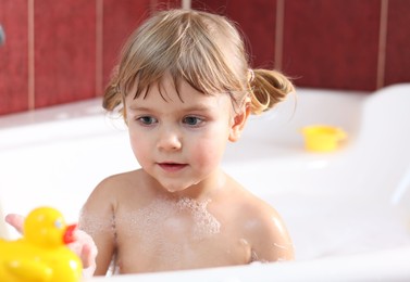 Photo of Little girl bathing with toy duck in tub at home, selective focus
