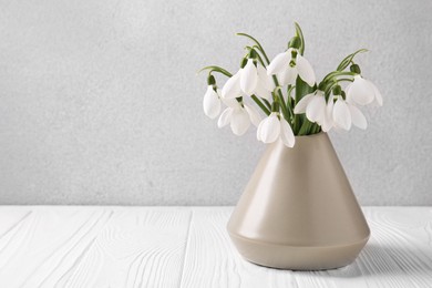 Beautiful snowdrops in vase on white wooden table, space for text