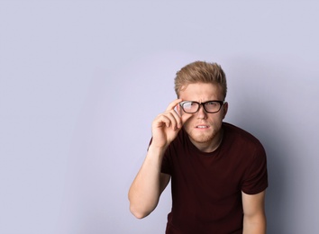 Young man with vision problem wearing glasses on light background