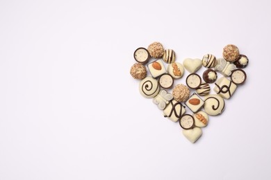 Heart made with delicious chocolate candies on white background, top view