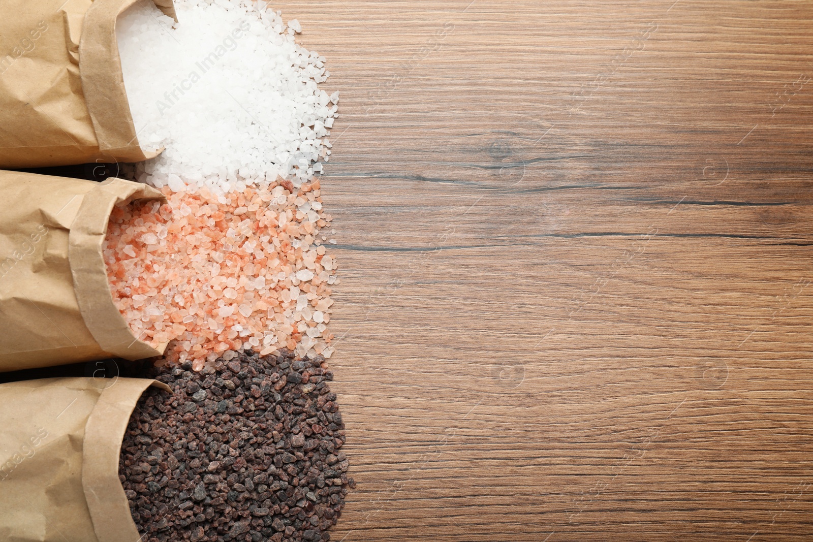 Photo of Paper bags with different kinds of salt on wooden table, flat lay. Space for text