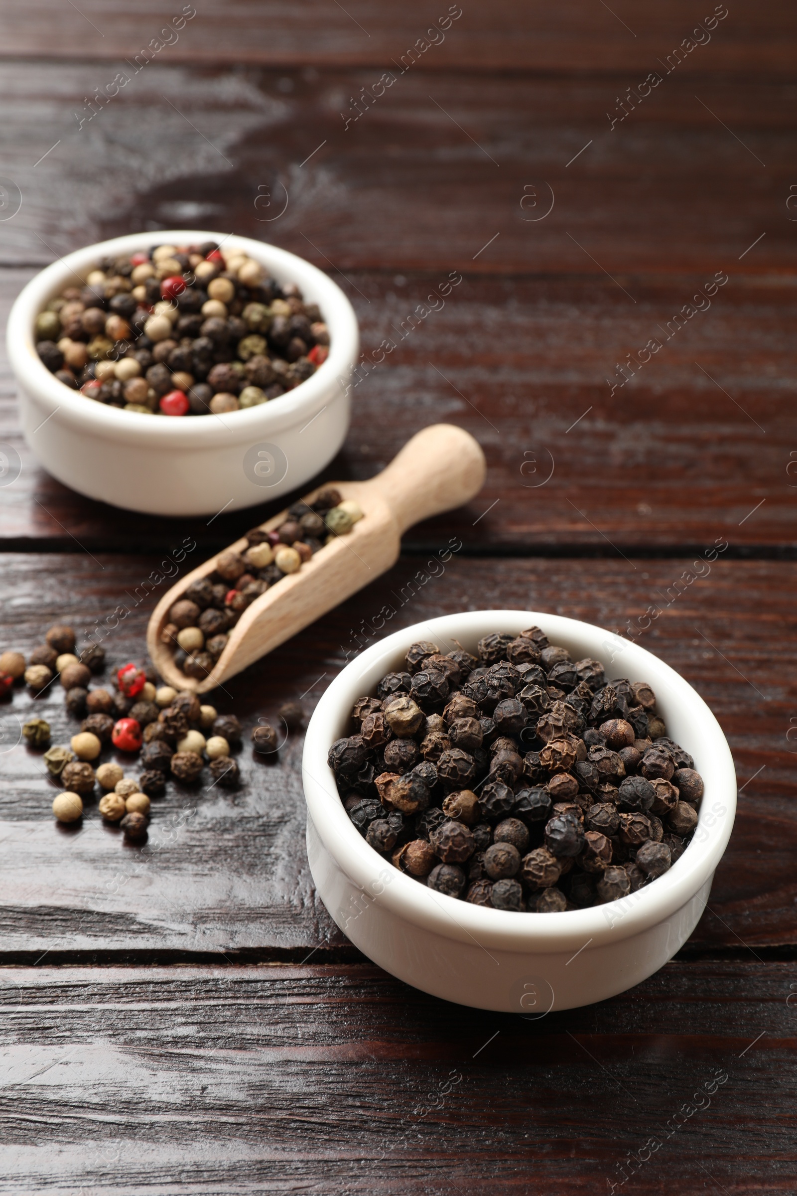 Photo of Aromatic spice. Different peppers in bowl and scoop on wooden table