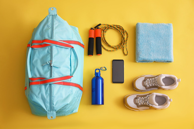 Gym bag, smartphone and sports equipment on yellow background, flat lay