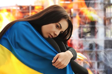 Image of Upset woman wrapped in national flag and ruined building on fire. Stop war in Ukraine