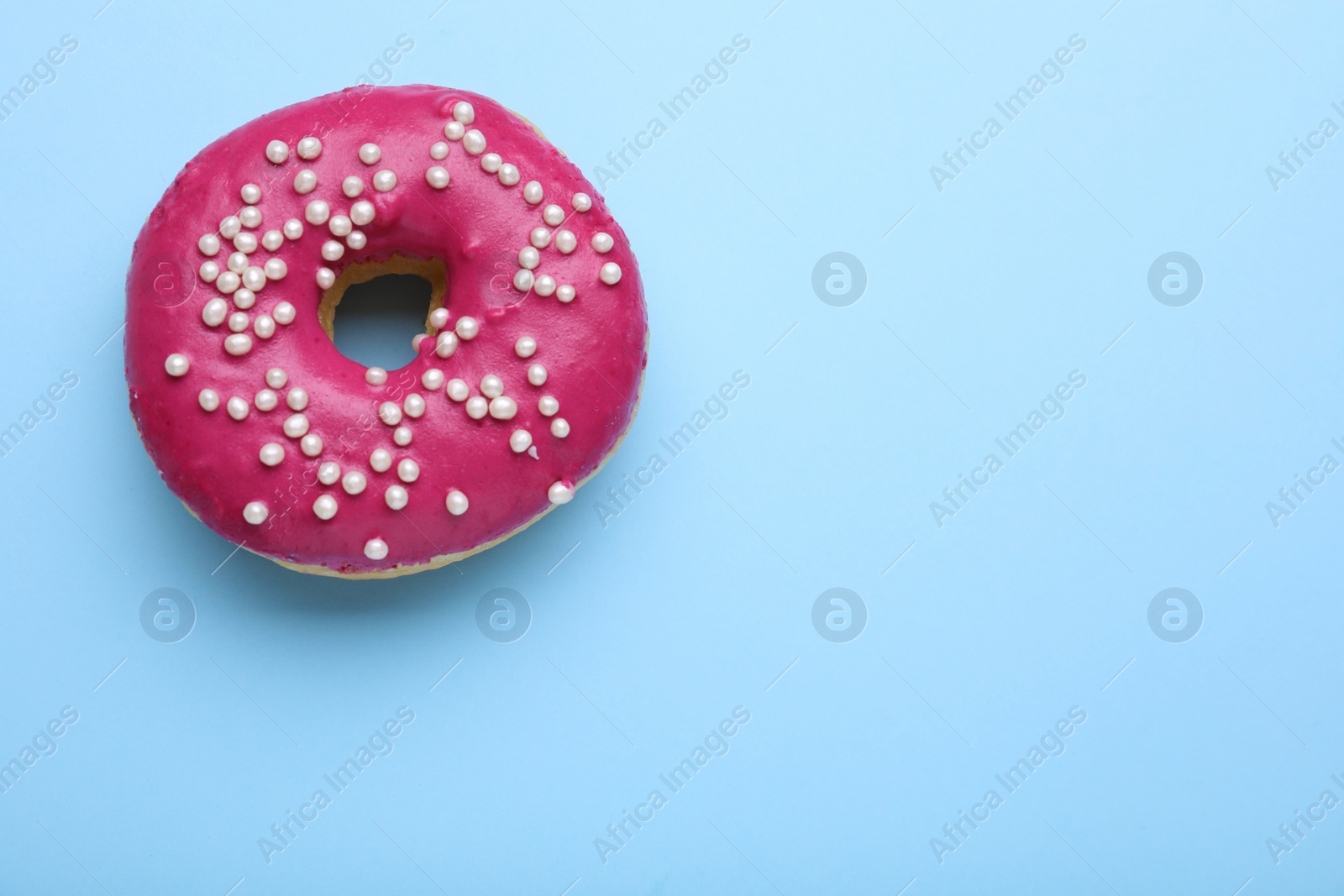 Photo of Tasty glazed donut decorated with sprinkles on light blue background, top view. Space for text
