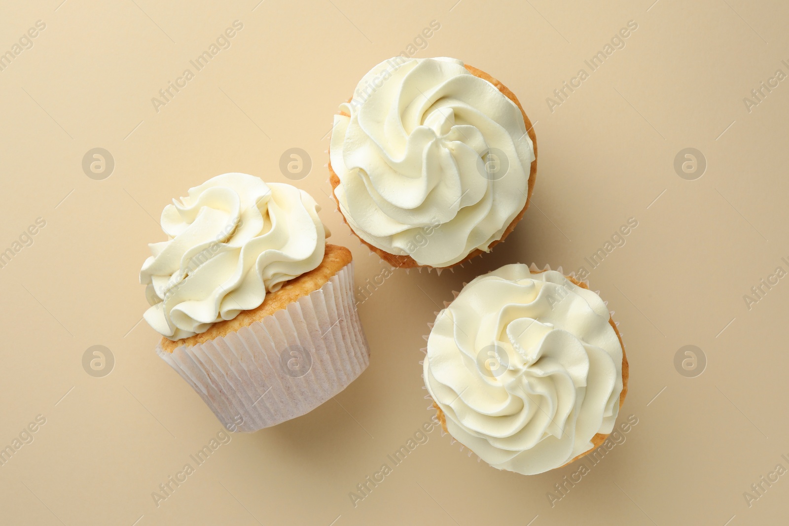 Photo of Tasty vanilla cupcakes with cream on beige background, top view