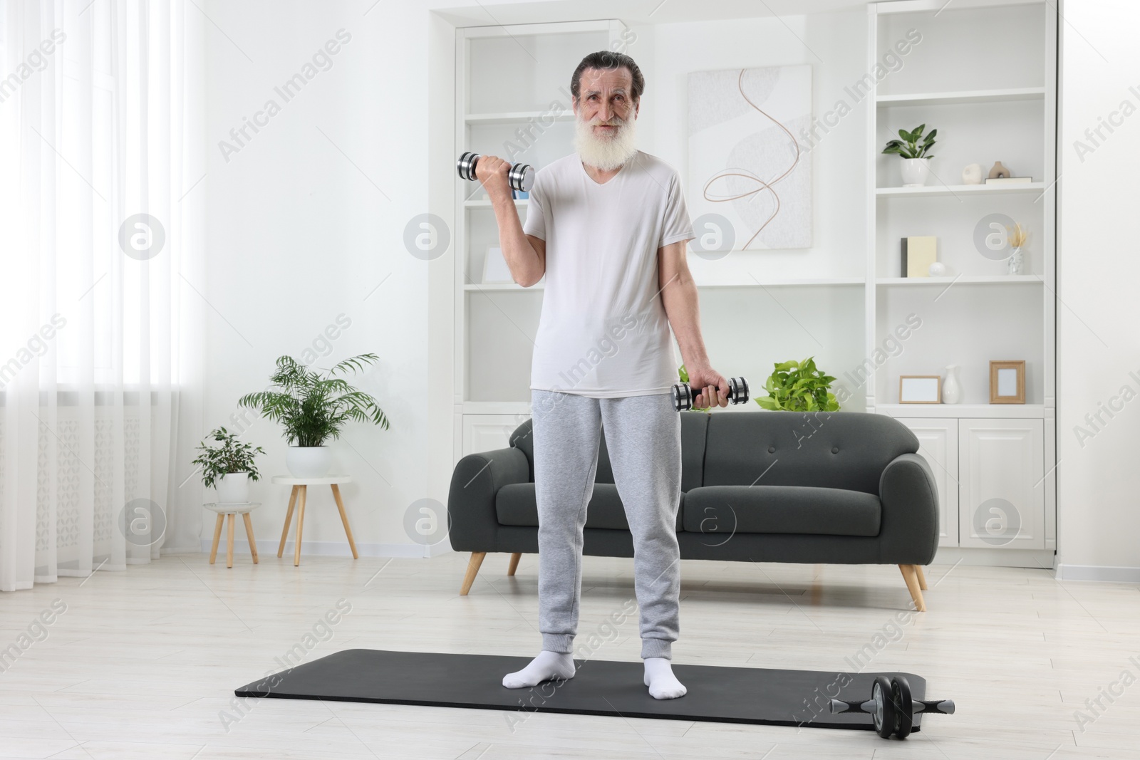 Photo of Senior man exercising with dumbbells on mat at home. Sports equipment