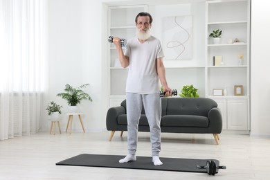 Photo of Senior man exercising with dumbbells on mat at home. Sports equipment