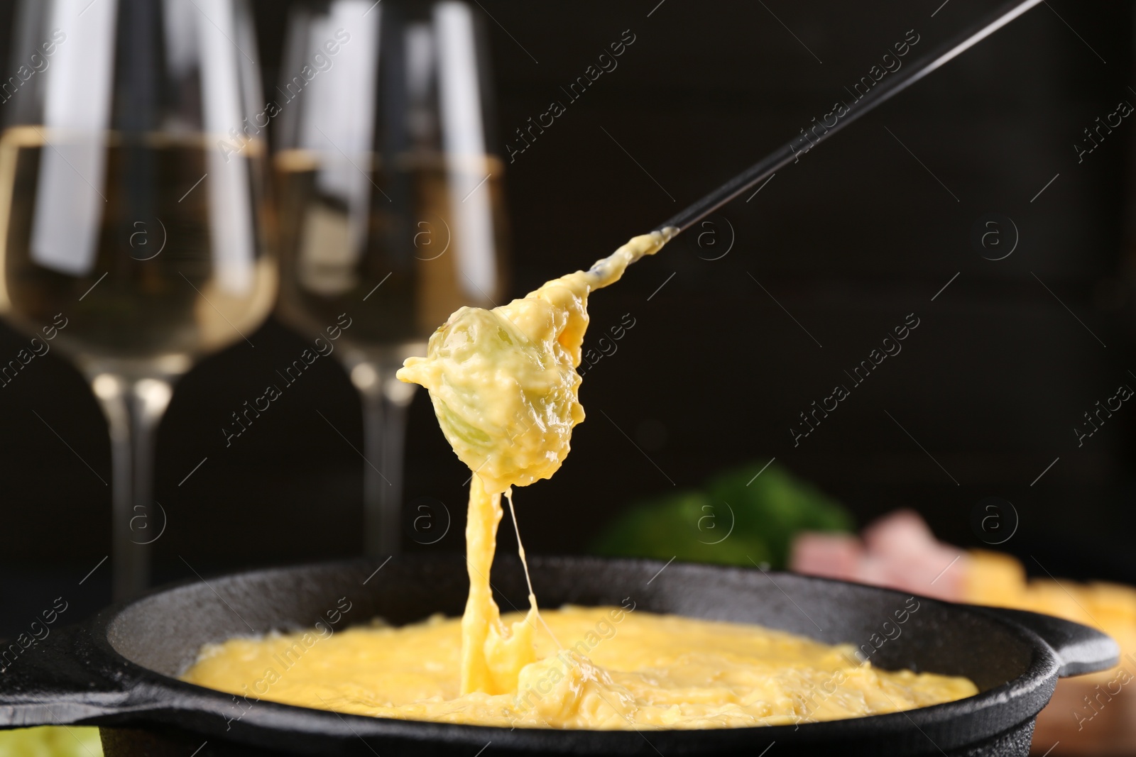 Photo of Dipping grape into fondue pot with melted cheese on table, closeup