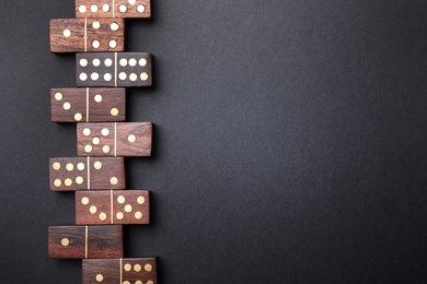 Photo of Wooden domino tiles on black background, flat lay. Space for text