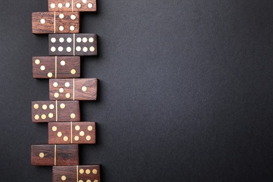 Wooden domino tiles on black background, flat lay. Space for text