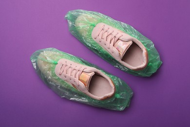 Photo of Sneakers in shoe covers on purple background, top view