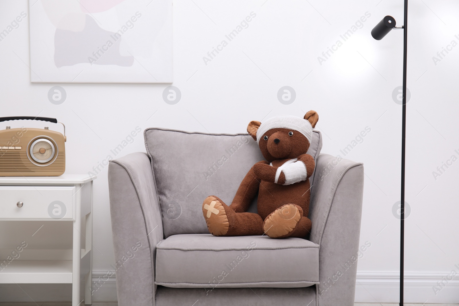 Photo of Toy bear with bandages sitting in armchair indoors