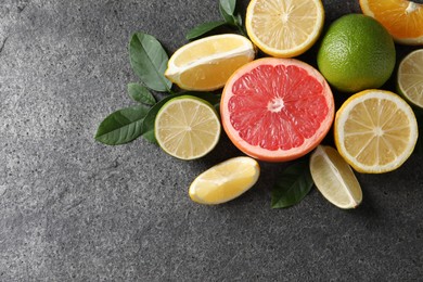 Photo of Different fresh citrus fruits and leaves on grey textured table, flat lay. Space for text