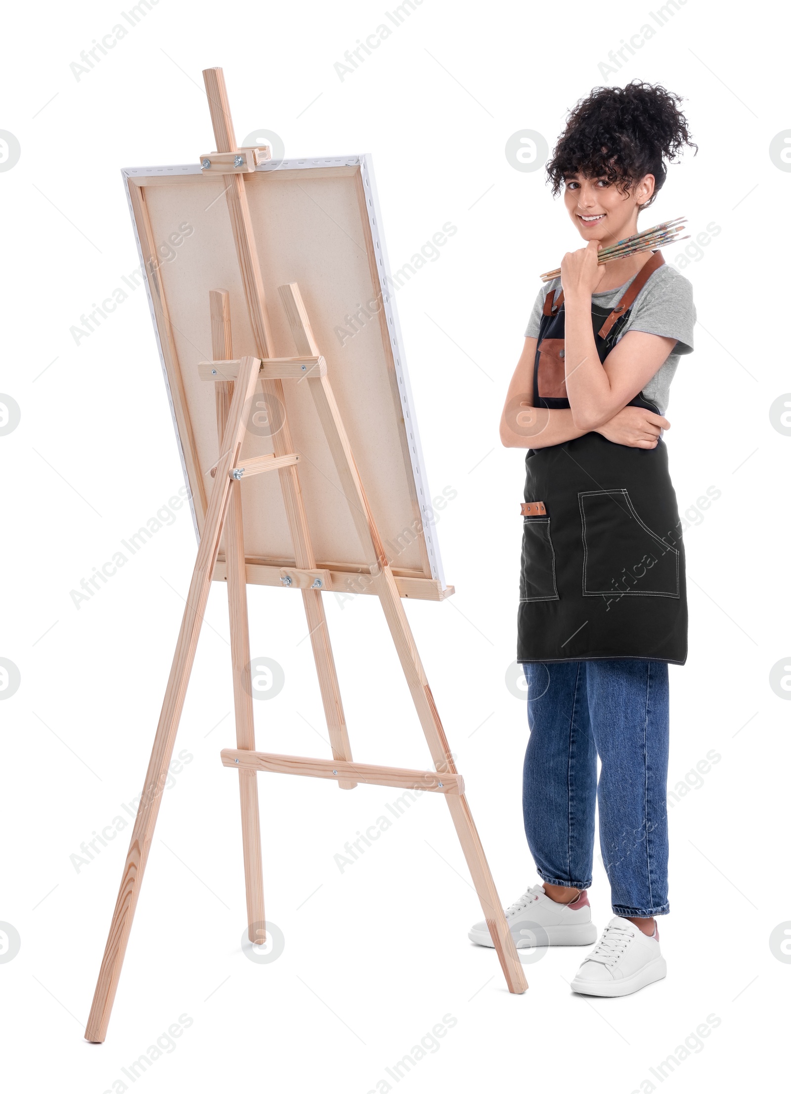 Photo of Young woman holding brush near easel with canvas against white background