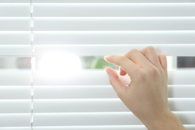 Photo of Young woman opening window blinds, closeup. Space for text