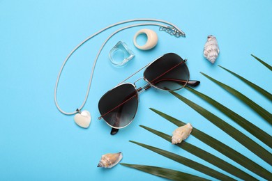 Stylish sunglasses, seashells and accessories on light blue background, flat lay
