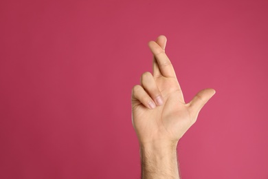 Photo of Man with crossed fingers and space for text on pink background, closeup. Superstition concept