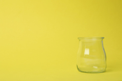 Photo of Open empty glass jar on light yellow background, space for text